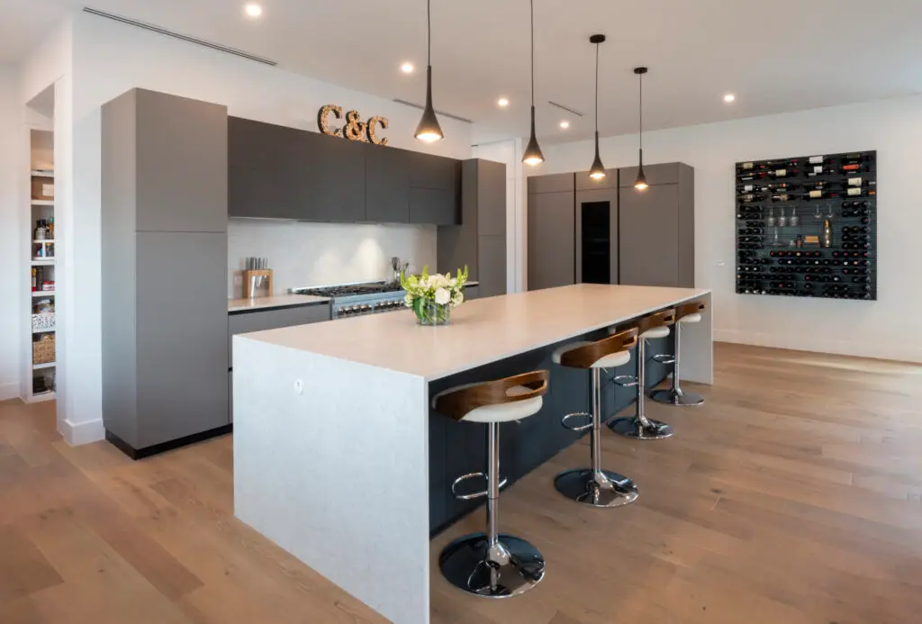 Modern kitchen interior with a central island, bar stools, and an elegant wine storage wall designed for flood and huricane resistance